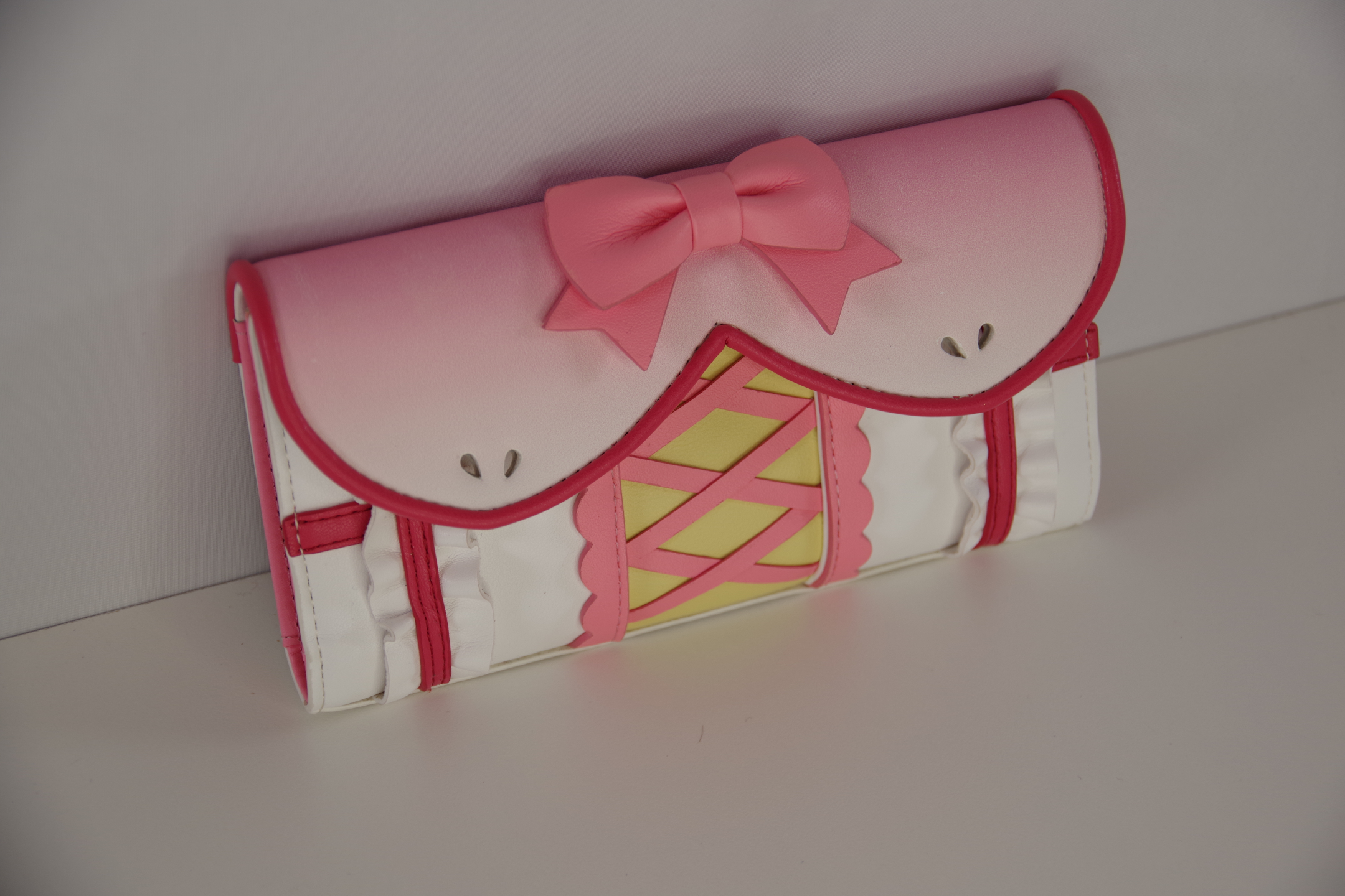 Angled view of a pink magical girl wallet featuring a bow accent, corset-inspired lacing, ruffle details, and kawaii anime fashion design.