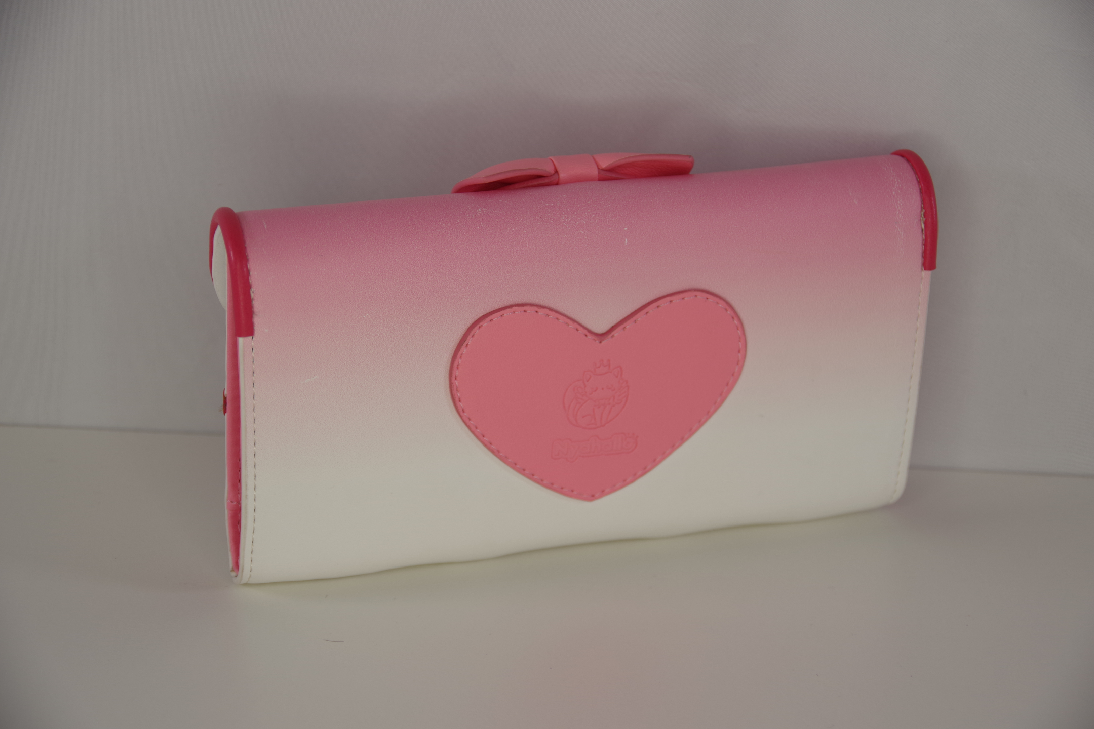 Back view of a pink magical girl inspired wallet featuring a heart-shaped logo detail and pastel pink to white gradient design.