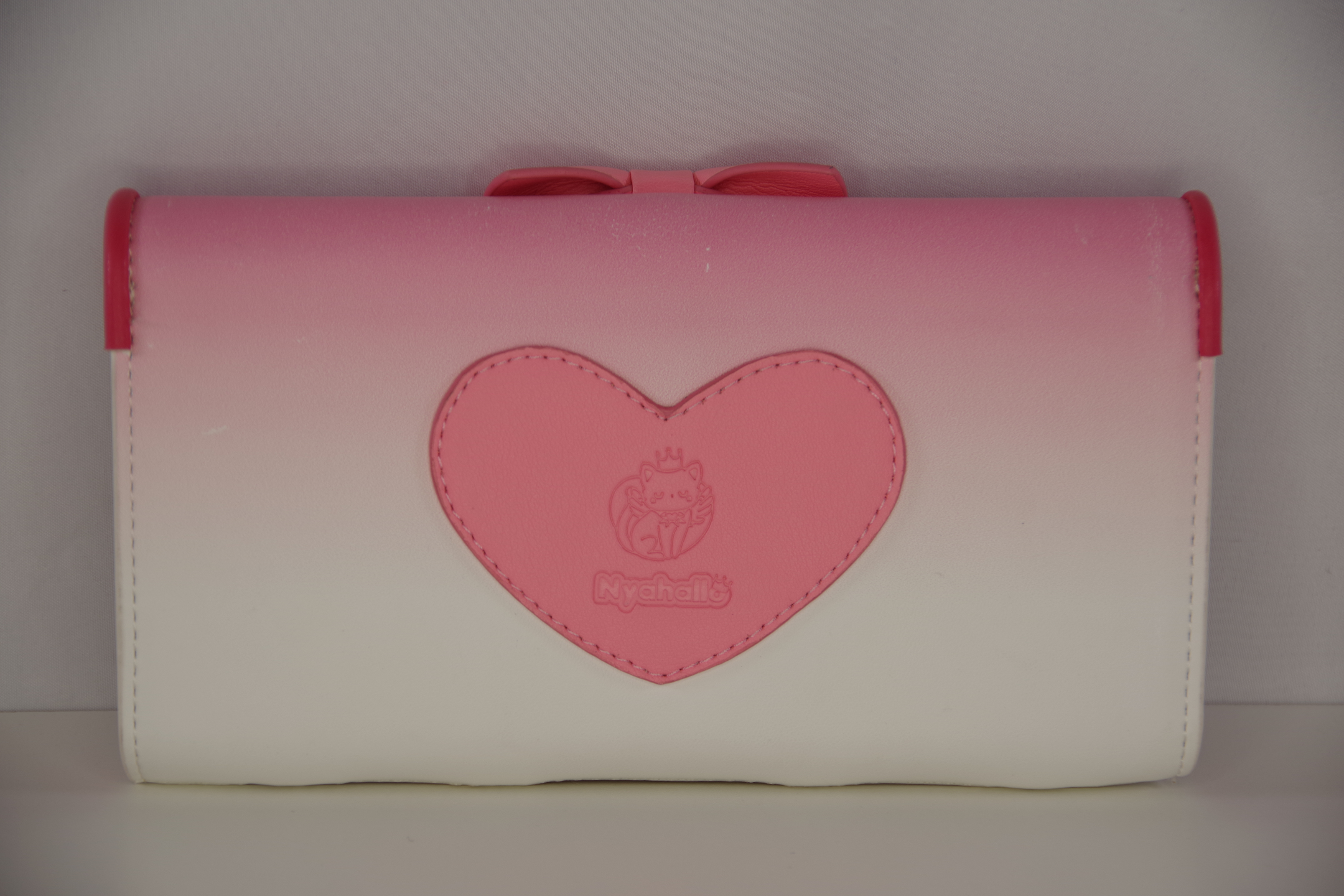 Back view of a pink magical girl inspired wallet featuring a heart-shaped logo applique and pastel pink to white gradient design.