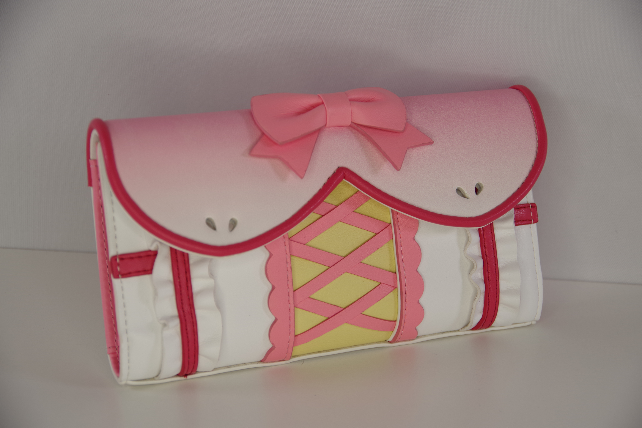 Pink magical girl inspired wallet with bow, corset-style lacing, and ruffle trim shown from a front angled view.