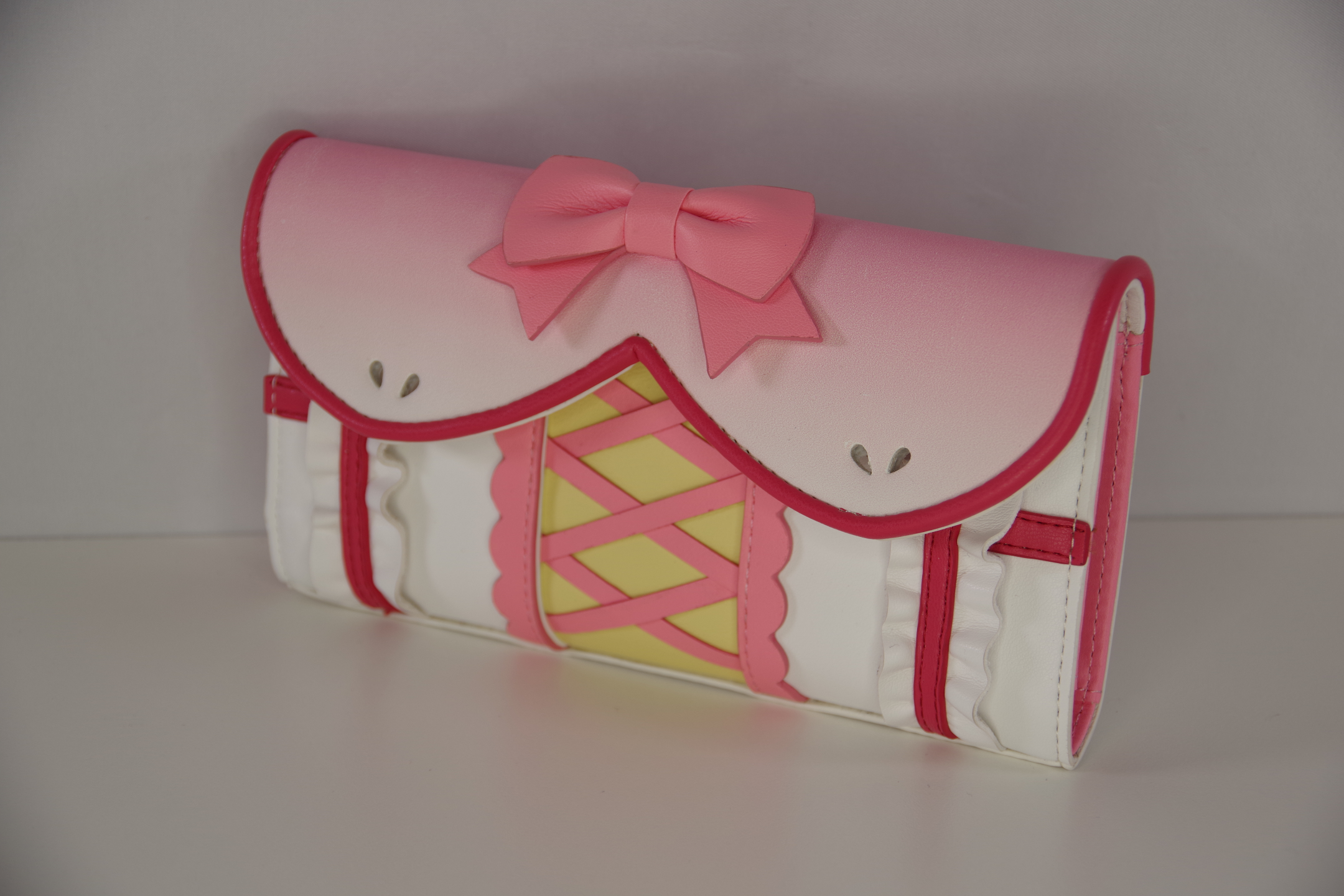 Pink magical girl inspired wallet with bow, corset-style lacing, ruffle trim, and pastel kawaii details shown from a right angled view.