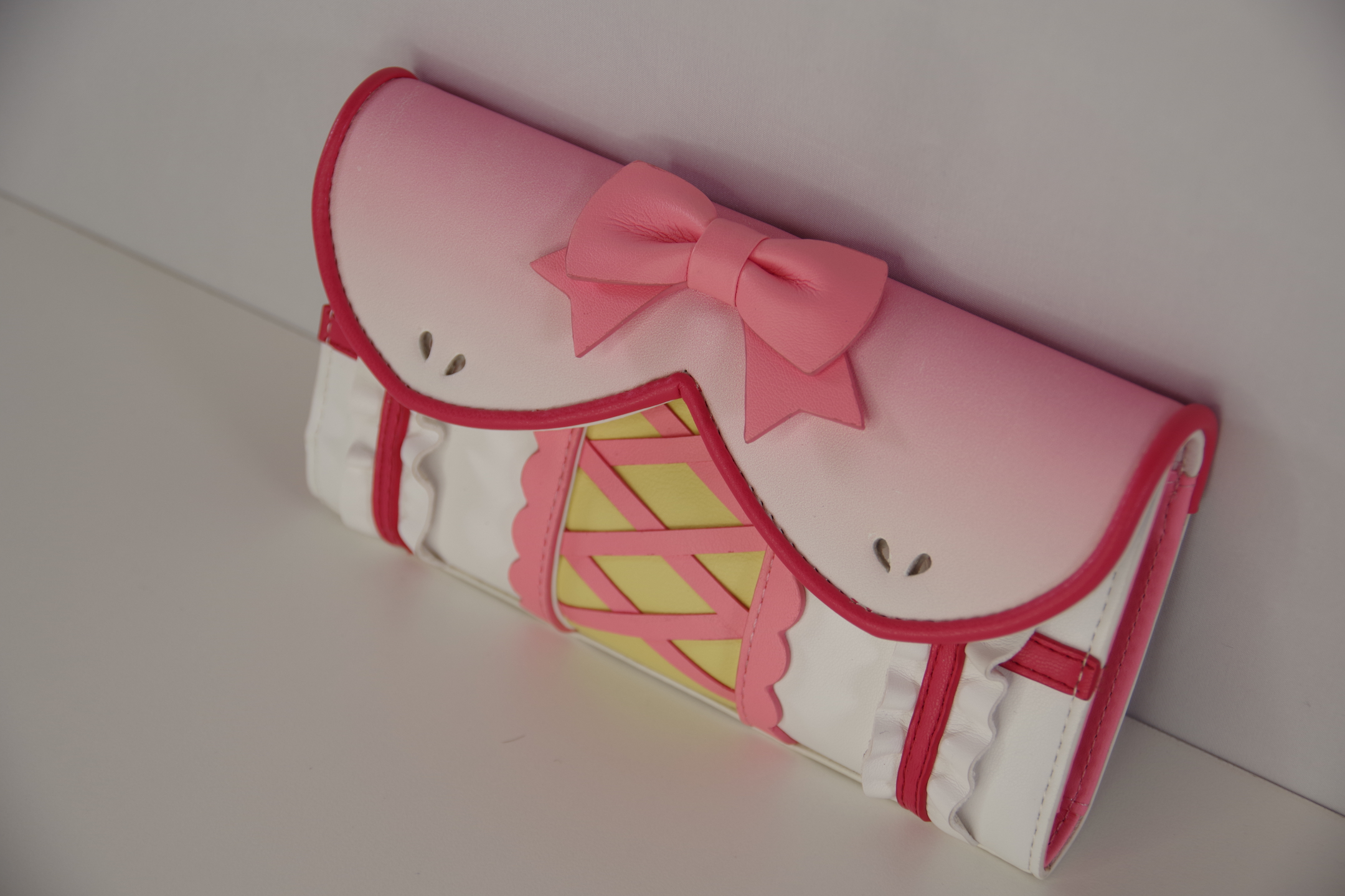 Three-quarter view of a pink magical girl inspired wallet featuring a bow accent, corset-style lacing, ruffle trim, and kawaii anime fashion details.