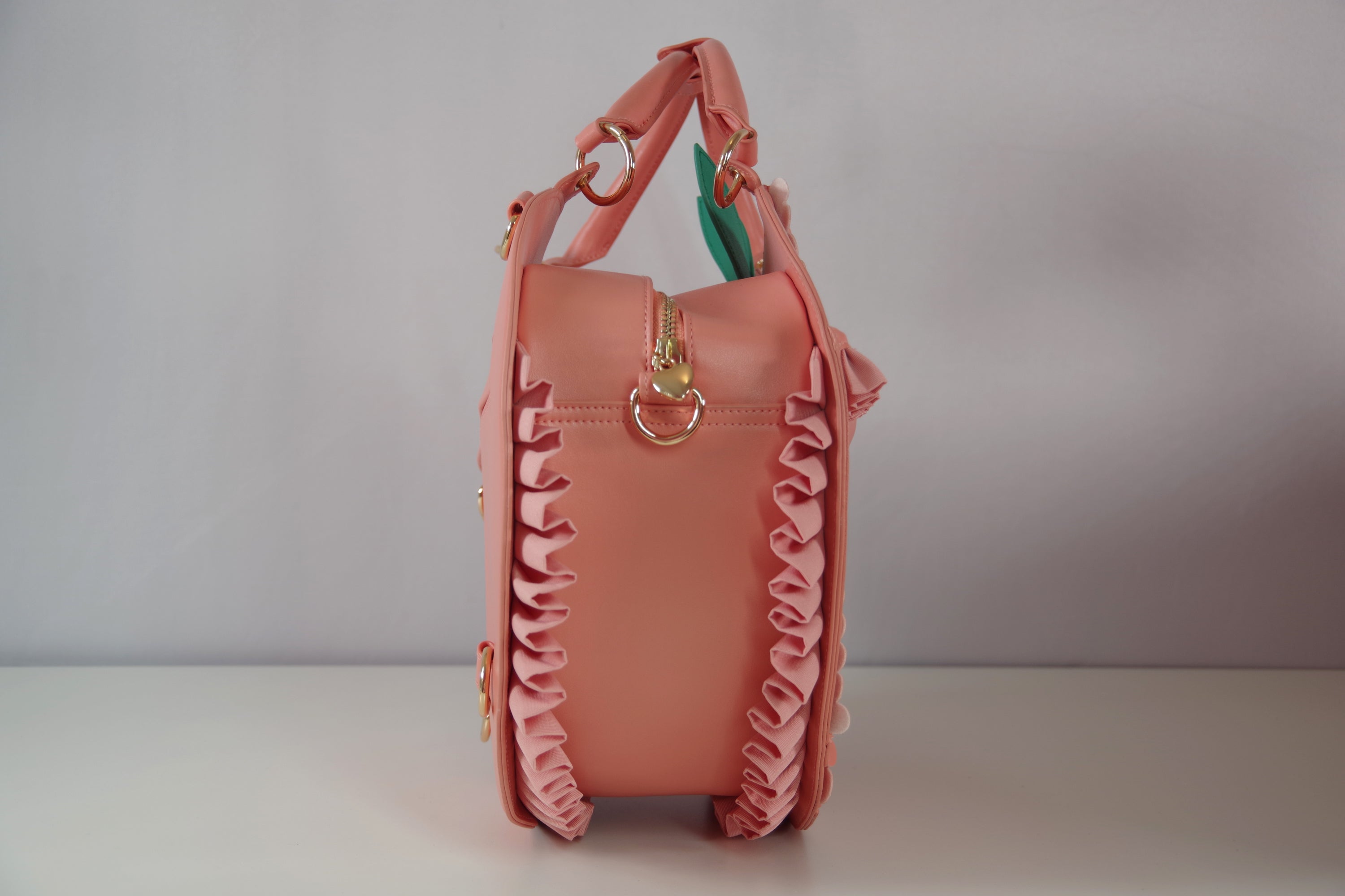 Side view of peach-shaped handbag showing ruffled trim, zipper closure, gold hardware, and spacious interior depth.