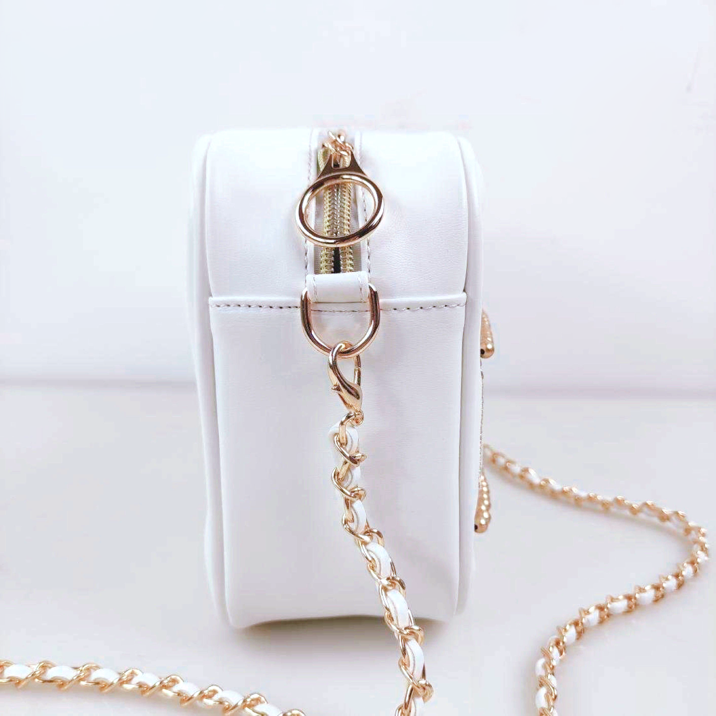 Side profile of a white celestial handbag featuring a gold chain strap, gold hardware, and compact crossbody design.